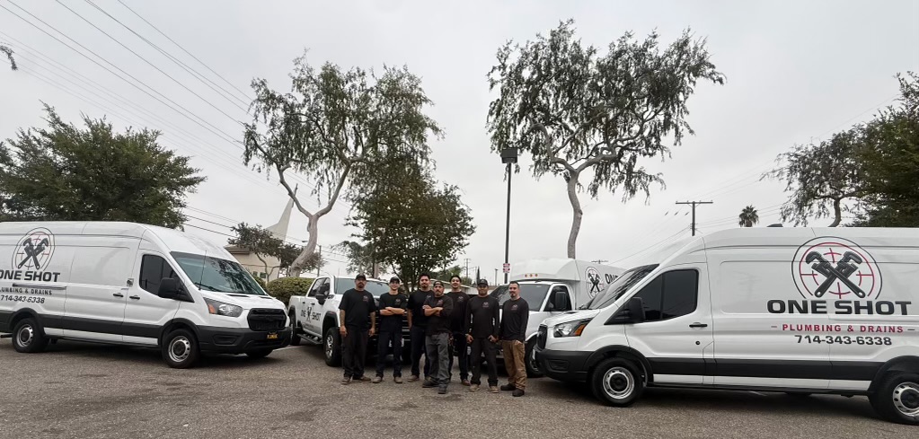 The real One Shot Plumbing and Drains crew standing together between their branded service trucks
